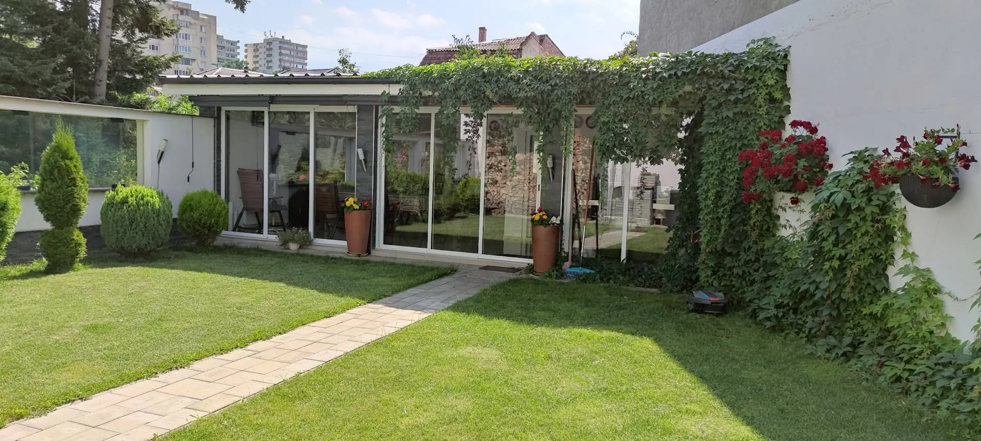 Terasă închisă cu sticlă, deschisă spre o grădină cu gazon